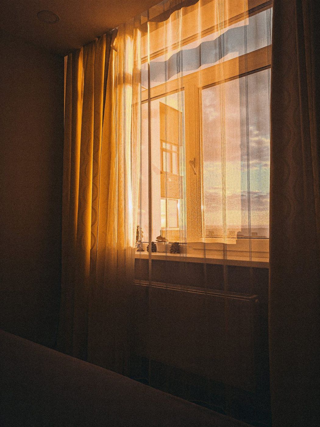 Warm sunlight passes through a sheer curtain with heavier curtains at the sides of a window.