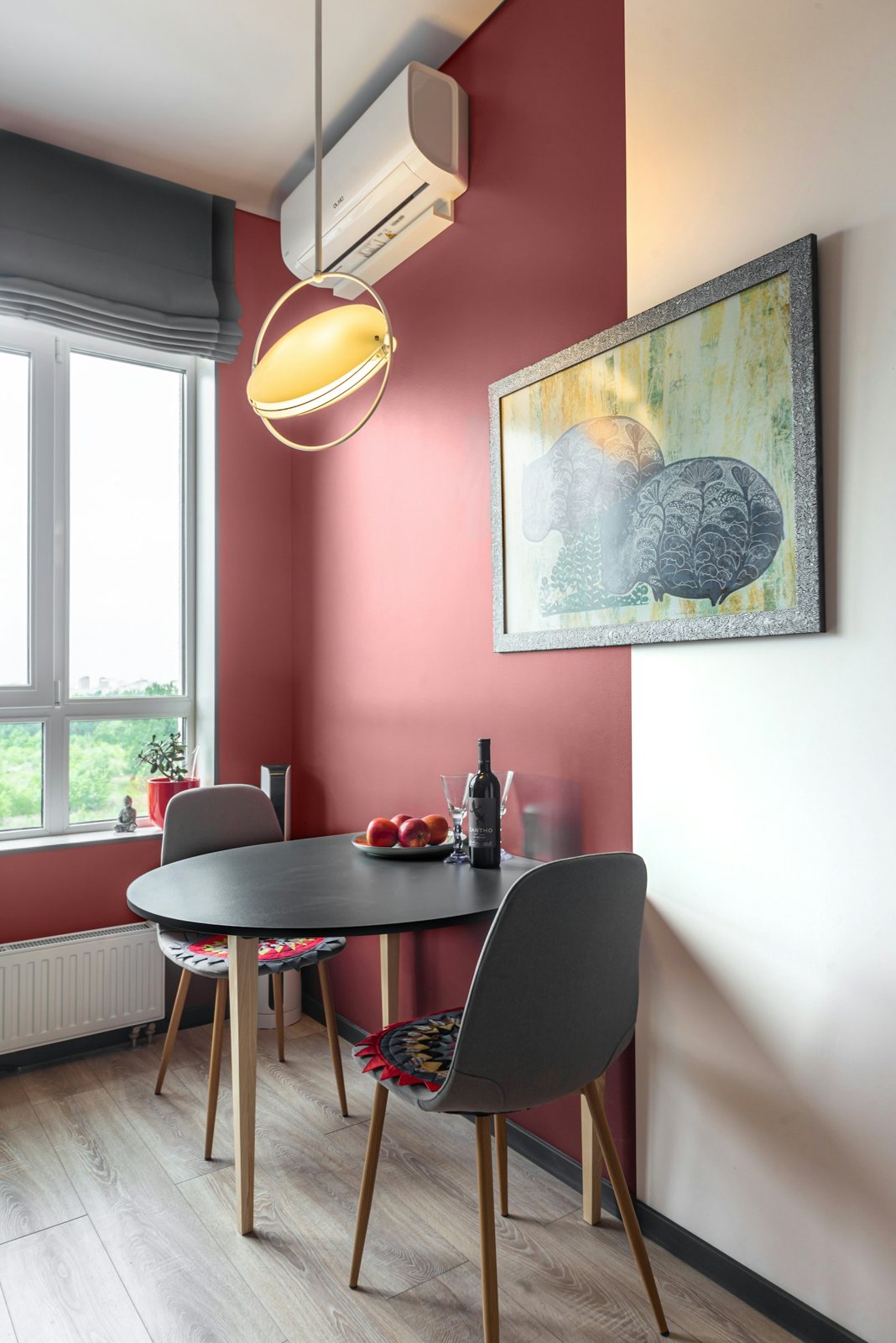 A small dark round dining table and two chairs beside a window and a red accent wall.