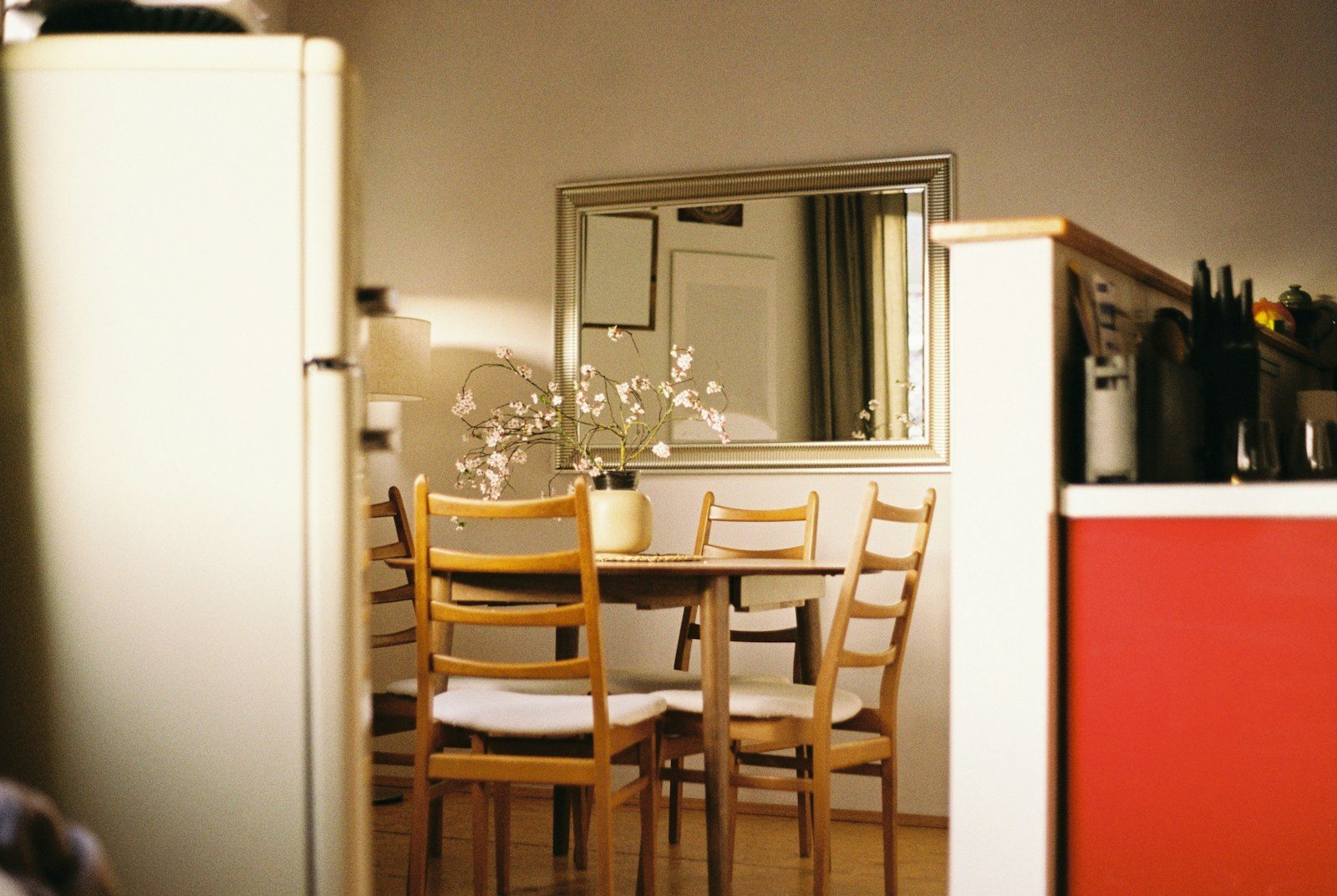 A wooden dining table with chairs between a refrigerator and a red kitchen cabinet.