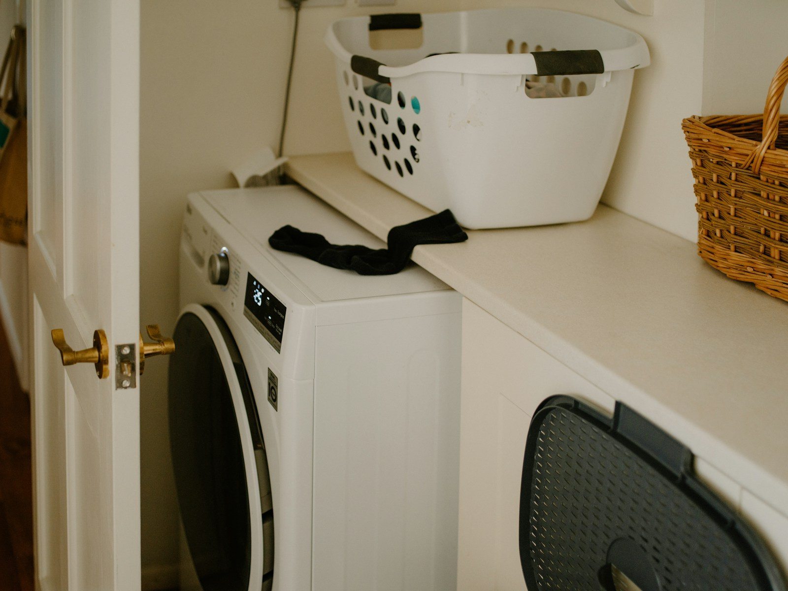 White laundry basket and a black sock above two laundry appliances in a compact utility space.