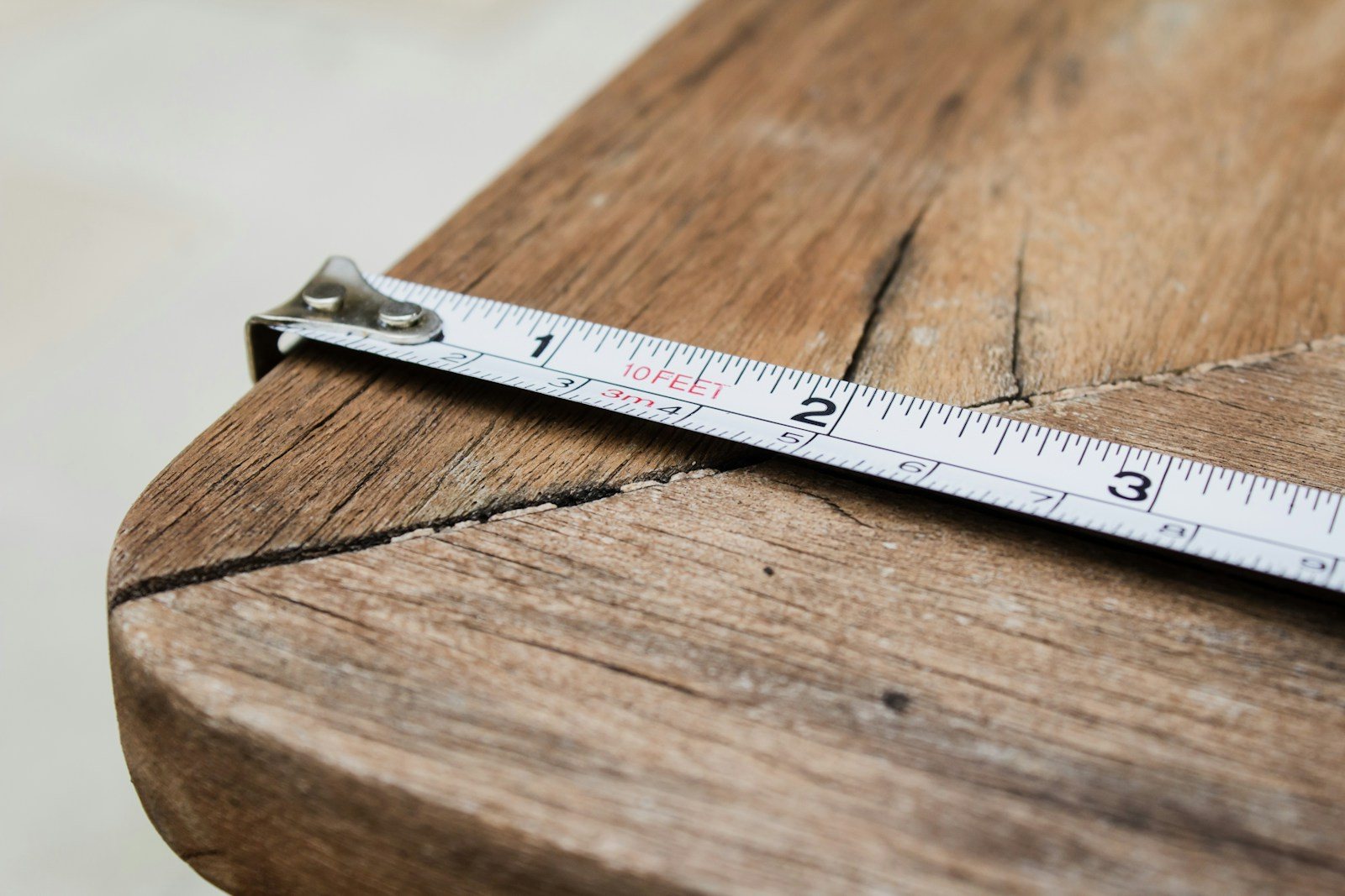 A metal measuring tape stretched across the rounded edge of a wooden table.