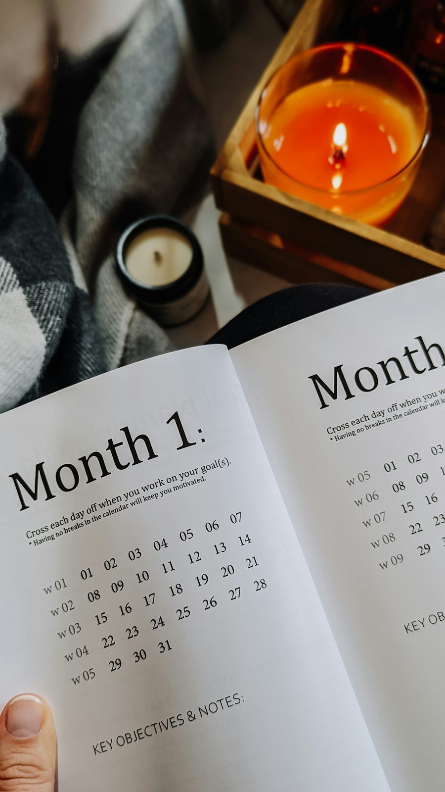 An open monthly planner held beside a lit amber candle on a tray.