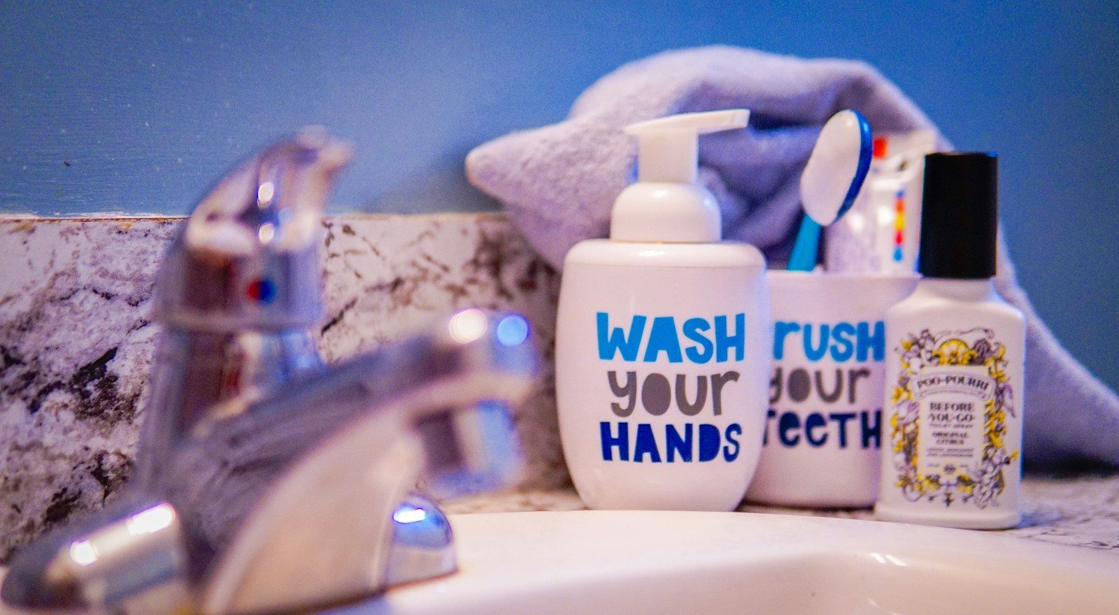 Bathroom sink with a silver faucet, soap pump, toothbrush cup and folded towel against a blue wall.