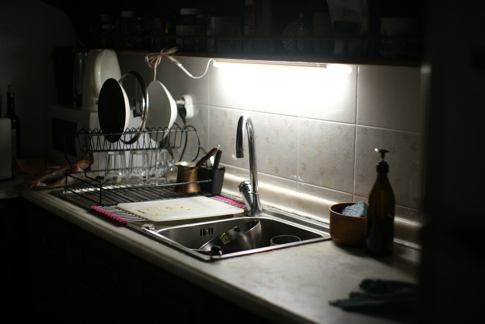 Dishes drying in a wire rack beside a stainless steel kitchen sink, cutting board and soap dispenser.