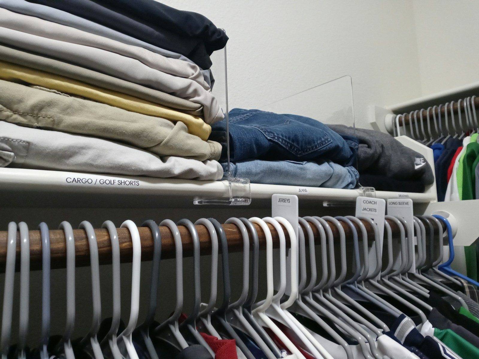 Folded trousers on a closet shelf above a crowded row of clothes hangers.