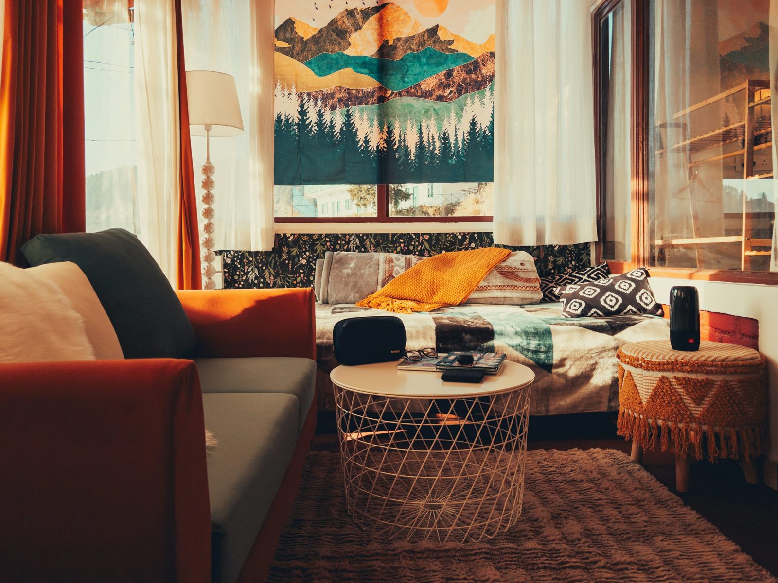 An orange-armed chair, a daybed, a wire coffee table and a fringed stool in a colorful sitting corner.