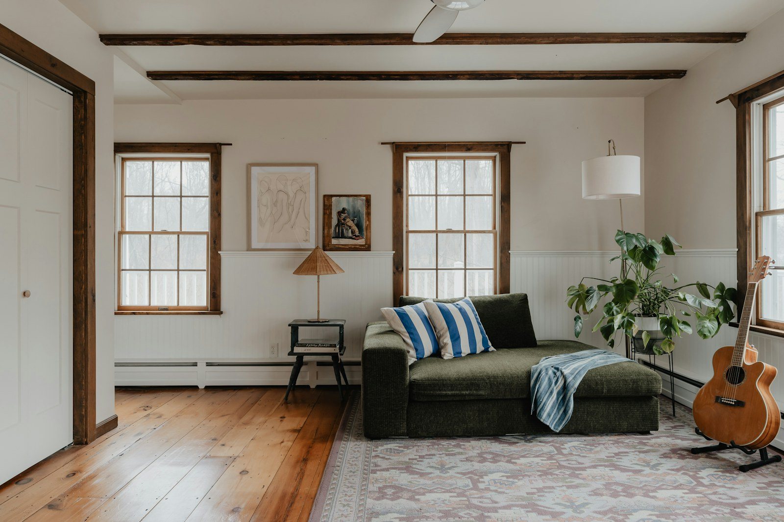 Sunlit living room with an olive green sofa, a guitar, wood floors and a patterned rug.